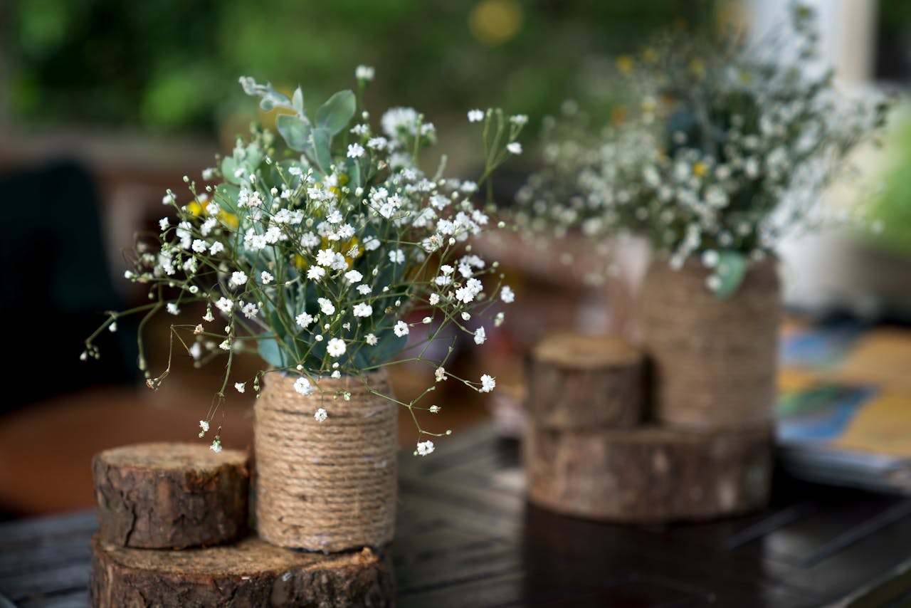 gallery-6 Rustic floral arrangement with white flowers in a twine-covered vase on a wooden base.